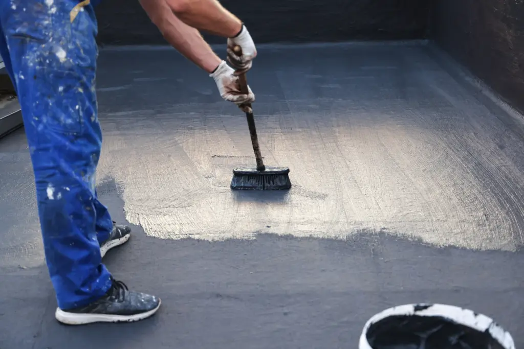 Wide-brush application of a dark external waterproof coating across a horizontal surface.