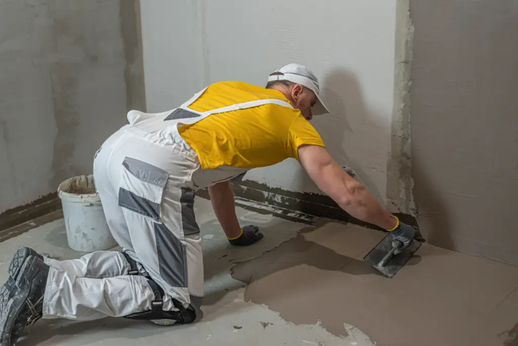 Tradesperson troweling self-levelling compound to smooth a concrete floor.