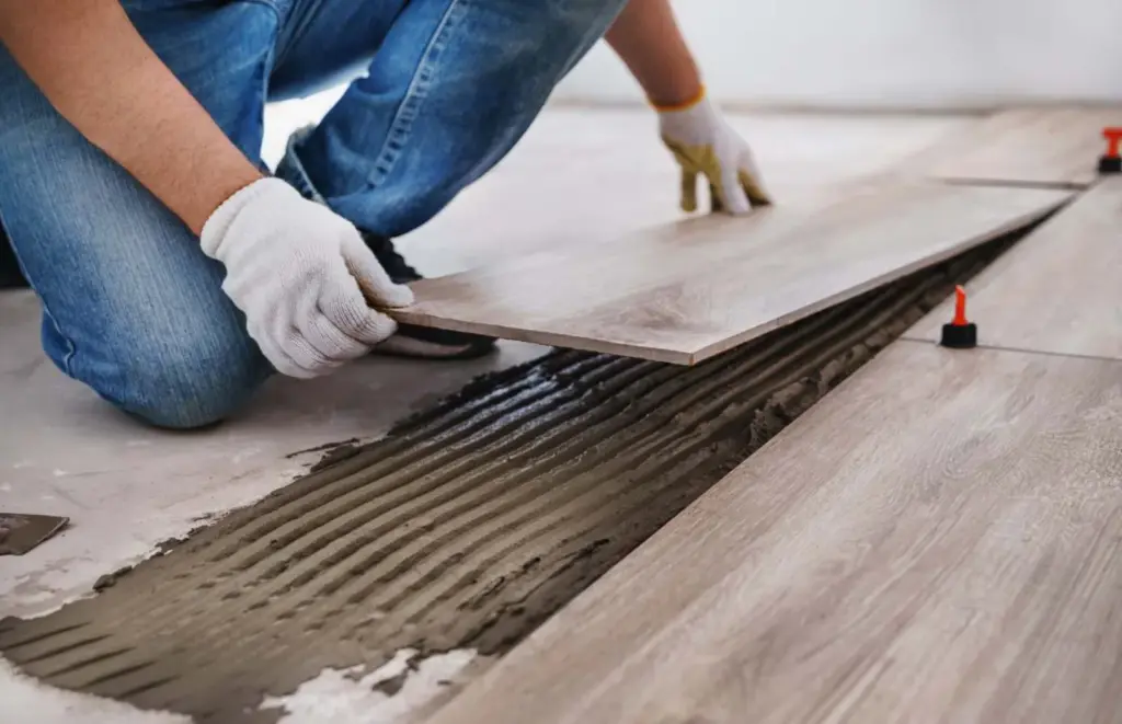 Tradesperson laying large-format tile onto fresh adhesive ribs with levelling clips.