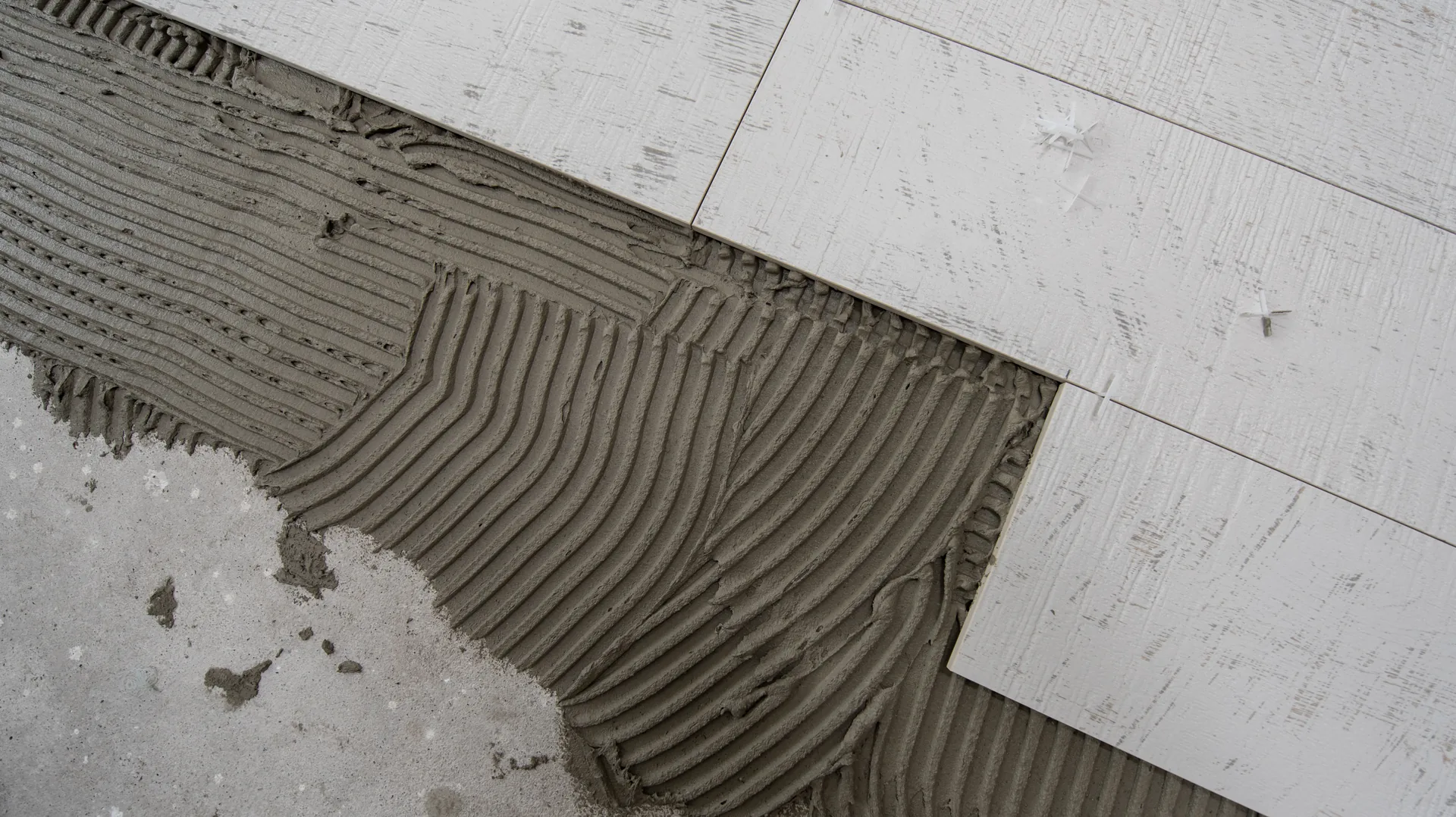 Trowel-combed tile adhesive ridges next to fresh timber-look plank tiles.