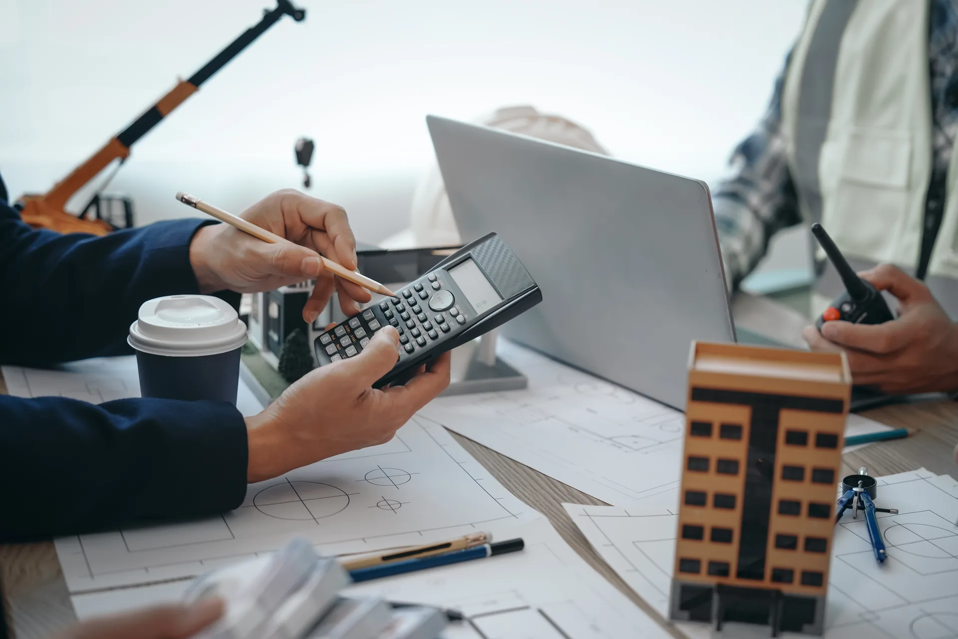 Hands using a calculator on architectural blueprints with a model building.