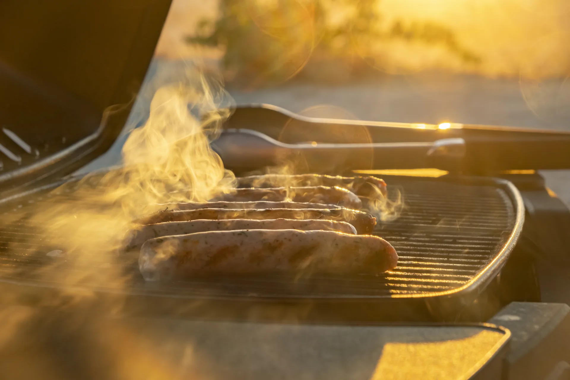 Sausages sizzling on a BBQ grill plate at golden sunset.