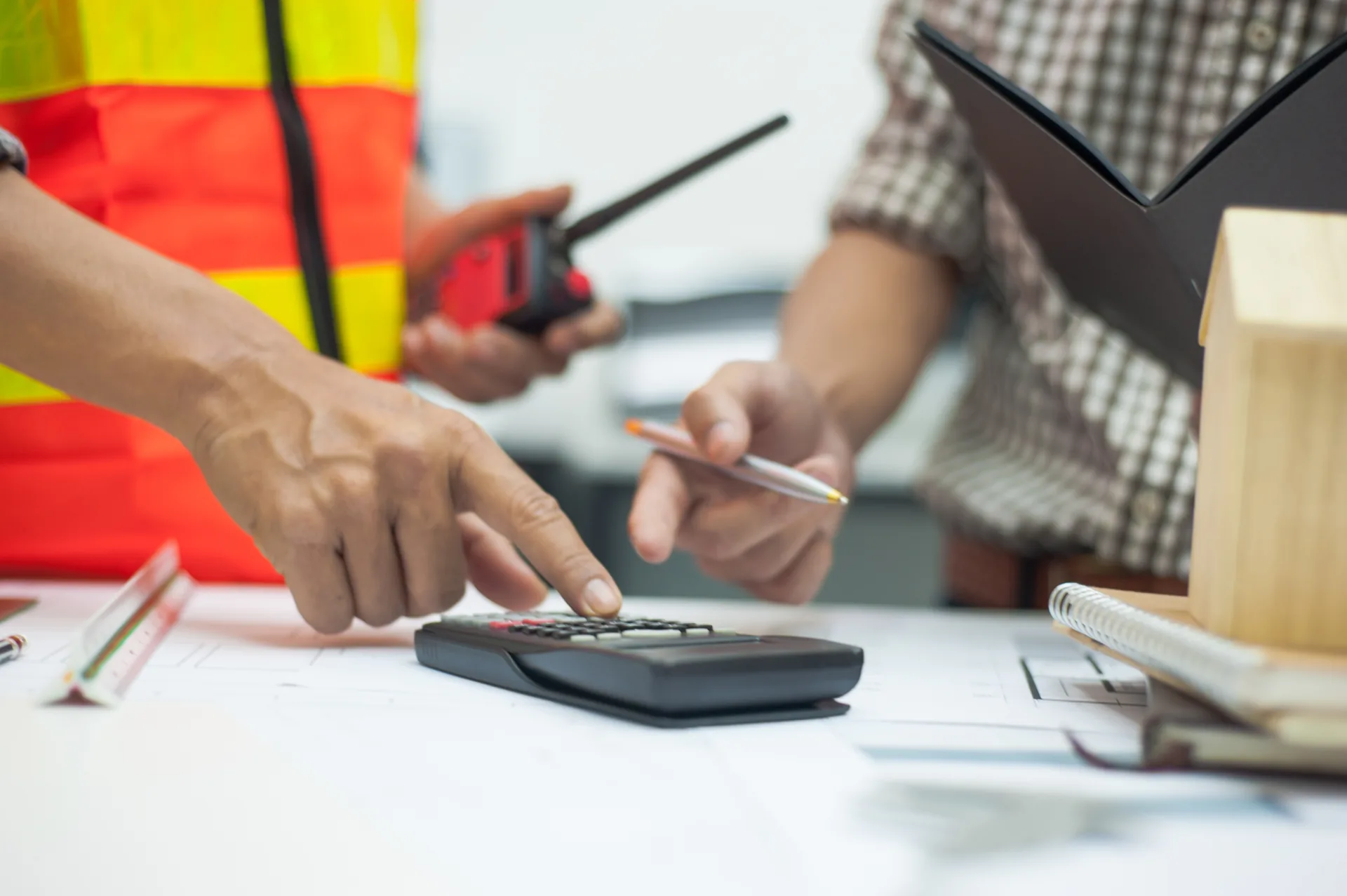 Hi-vis tradie using a calculator over building paperwork.