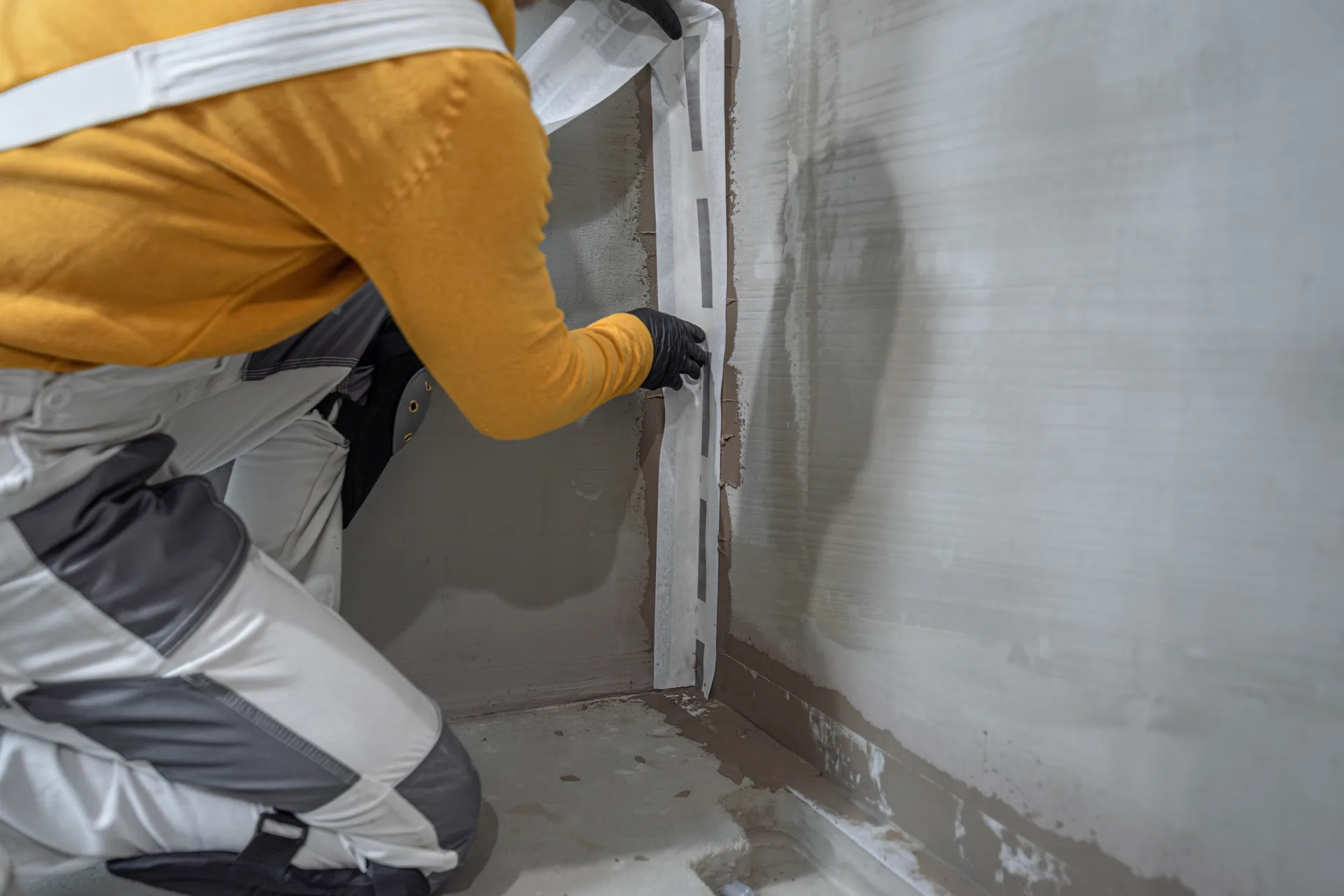 Tradie installing reinforcing membrane tape at an internal wall corner.